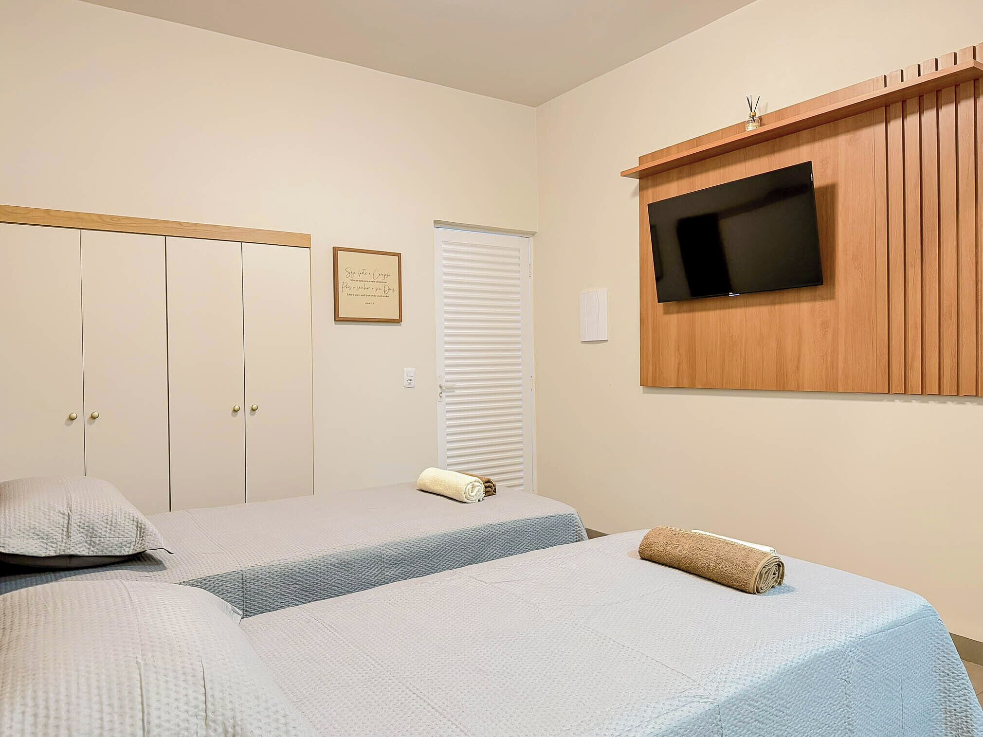 Un dormitorio con una cama, un televisor montado en un panel de madera, un armario y un letrero enmarcado en la pared.