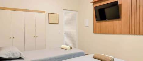 A bedroom with a bed, a TV mounted on a wooden panel, a wardrobe, and a framed sign on the wall.