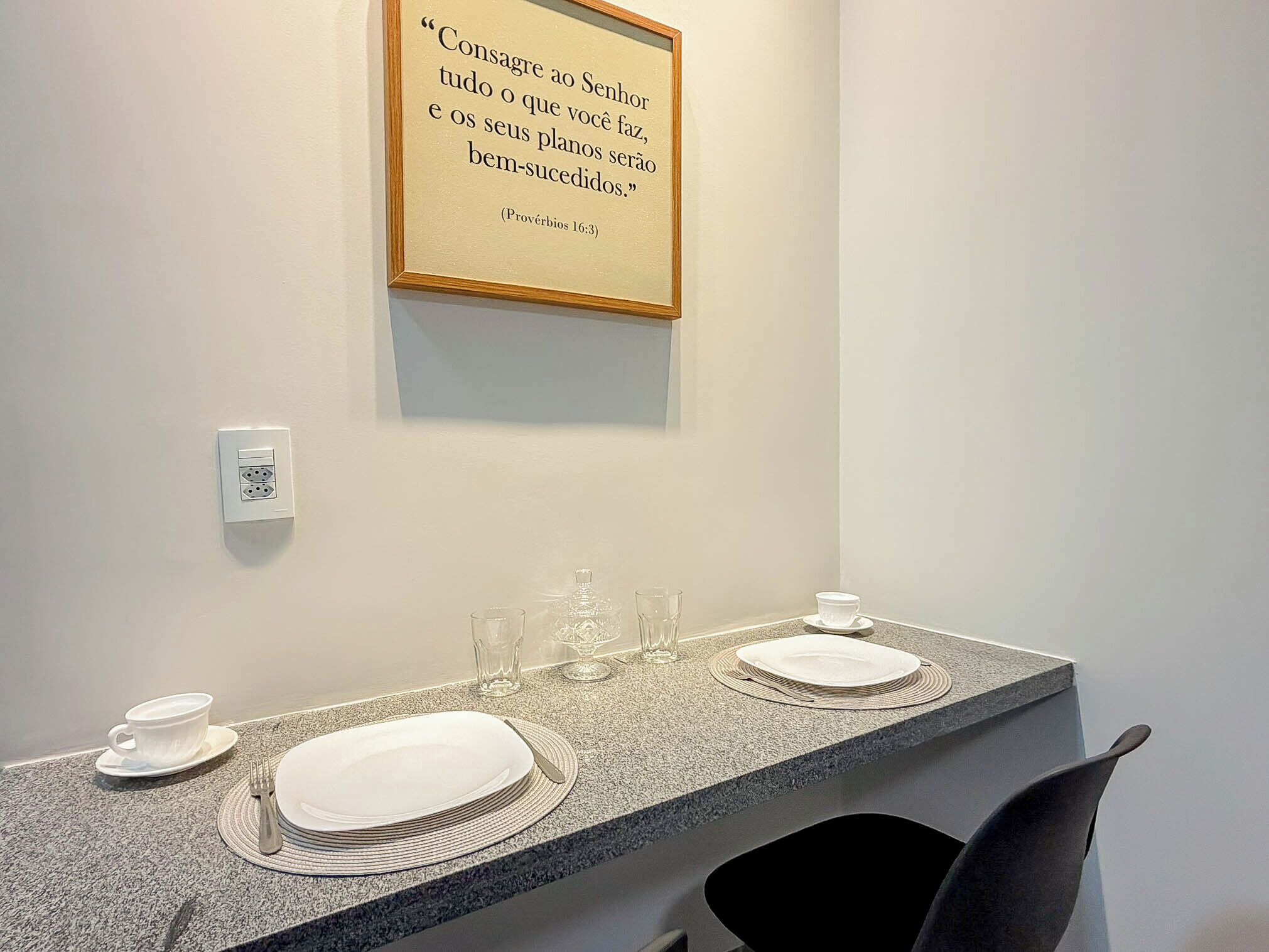 A hotel bathroom with a granite countertop, a framed quote on the wall, and a mirror.