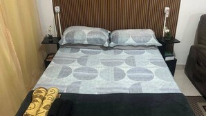 A bed with a patterned bedspread, two pillows, a black blanket, and rolled towels on a bedside table. - Lapa Heart Studio (Rio de Janeiro)