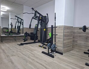 A gym with various exercise equipment, including a bench press, squat rack, and weight bench. - Playa del Cura Spa Retreat (Torrevieja)