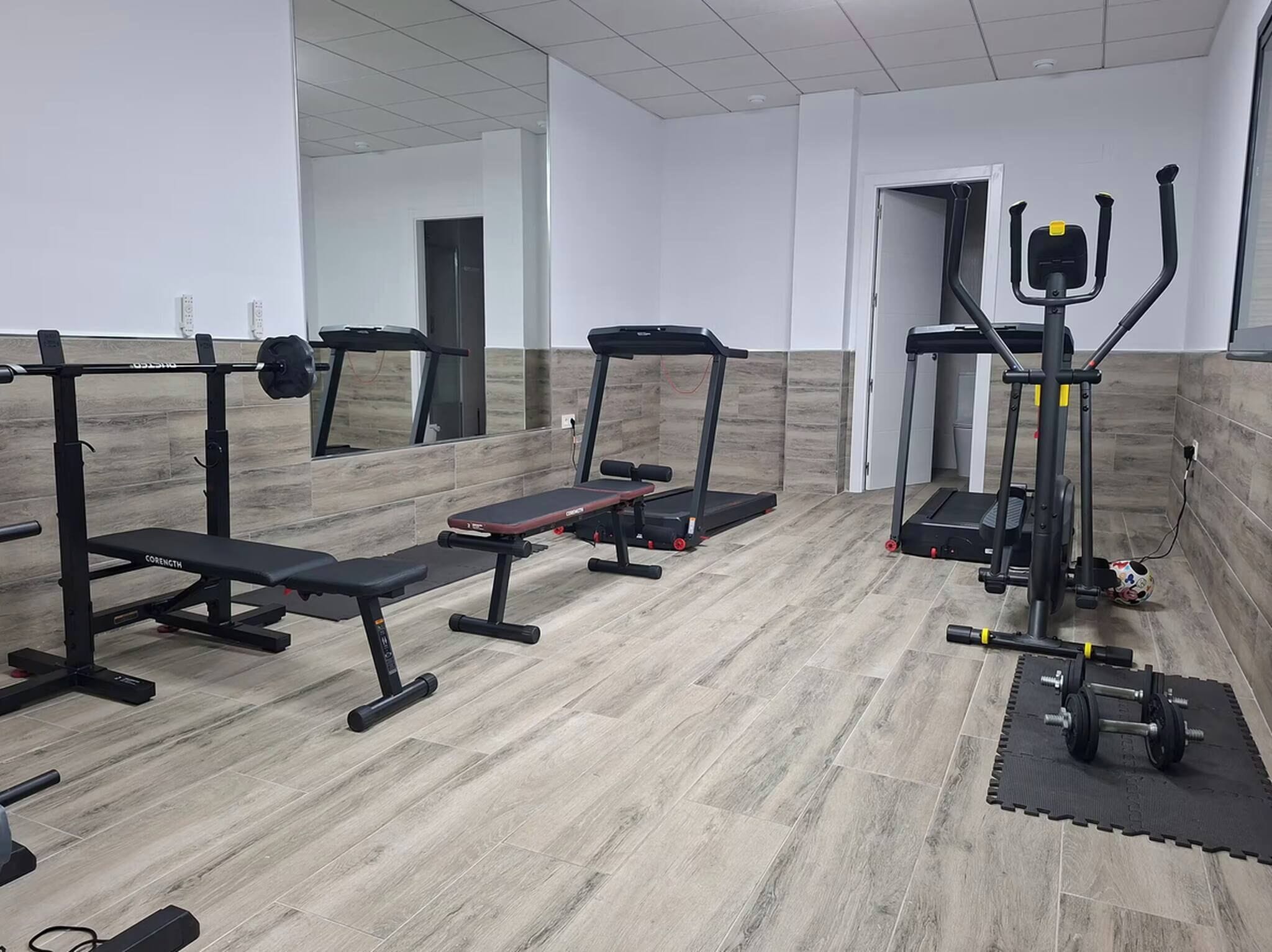 A gym with various exercise equipment, including treadmills, a bench press, and free weights.