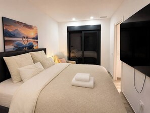 Quarto com cama, televisão, quadro e porta de correr.