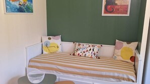 Une chambre avec un lit simple, un mur vert, un lit avec une literie à rayures, une petite table avec une chaise et une affiche accrochée au mur.