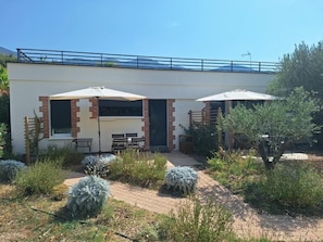 Eine moderne Terrassenanlage im Freien mit einer Sitzecke, zwei Sonnenschirmen und einem Weg zu einem Gebäude mit einem blauen Geländer.