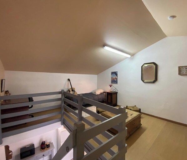 Um quarto com uma cama de solteiro, um violão, uma mesa de cabeceira e um quadro na parede.
