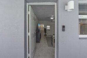 A hallway with a door leading to a bathroom, a ceiling fan, and a wall-mounted light fixture. - LaPlaya Pompano Private Beach + Pool (Pompano Beach)