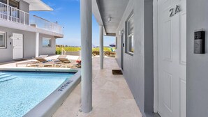 A pool area with lounge chairs, a swimming pool, and a building with a balcony. - LaPlaya Pompano Private Beach + Pool (Pompano Beach)