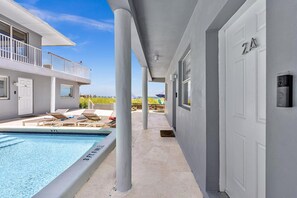 A pool area with lounge chairs, a swimming pool, and a building with a balcony. - LaPlaya Pompano Private Beach + Pool (Pompano Beach)