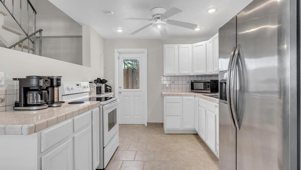 A modern kitchen with white cabinets, stainless steel appliances, and a ceiling fan. - LaPlaya Pompano Private Beach + Pool (Pompano Beach)