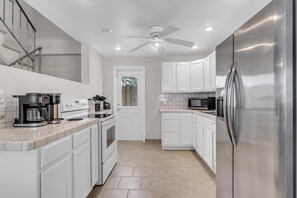A modern kitchen with white cabinets, stainless steel appliances, and a ceiling fan. - LaPlaya Pompano Private Beach + Pool (Pompano Beach)