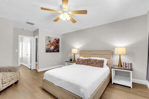 A bedroom with a large bed, two bedside tables with lamps, a ceiling fan, a door, and a wall-mounted artwork. - LaPlaya Pompano Private Beach + Pool (Pompano Beach)