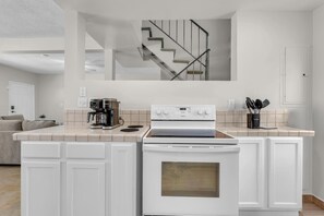 A modern kitchen with white cabinetry, a built-in oven, a coffee maker, and a stove. - LaPlaya Pompano Private Beach + Pool (Pompano Beach)