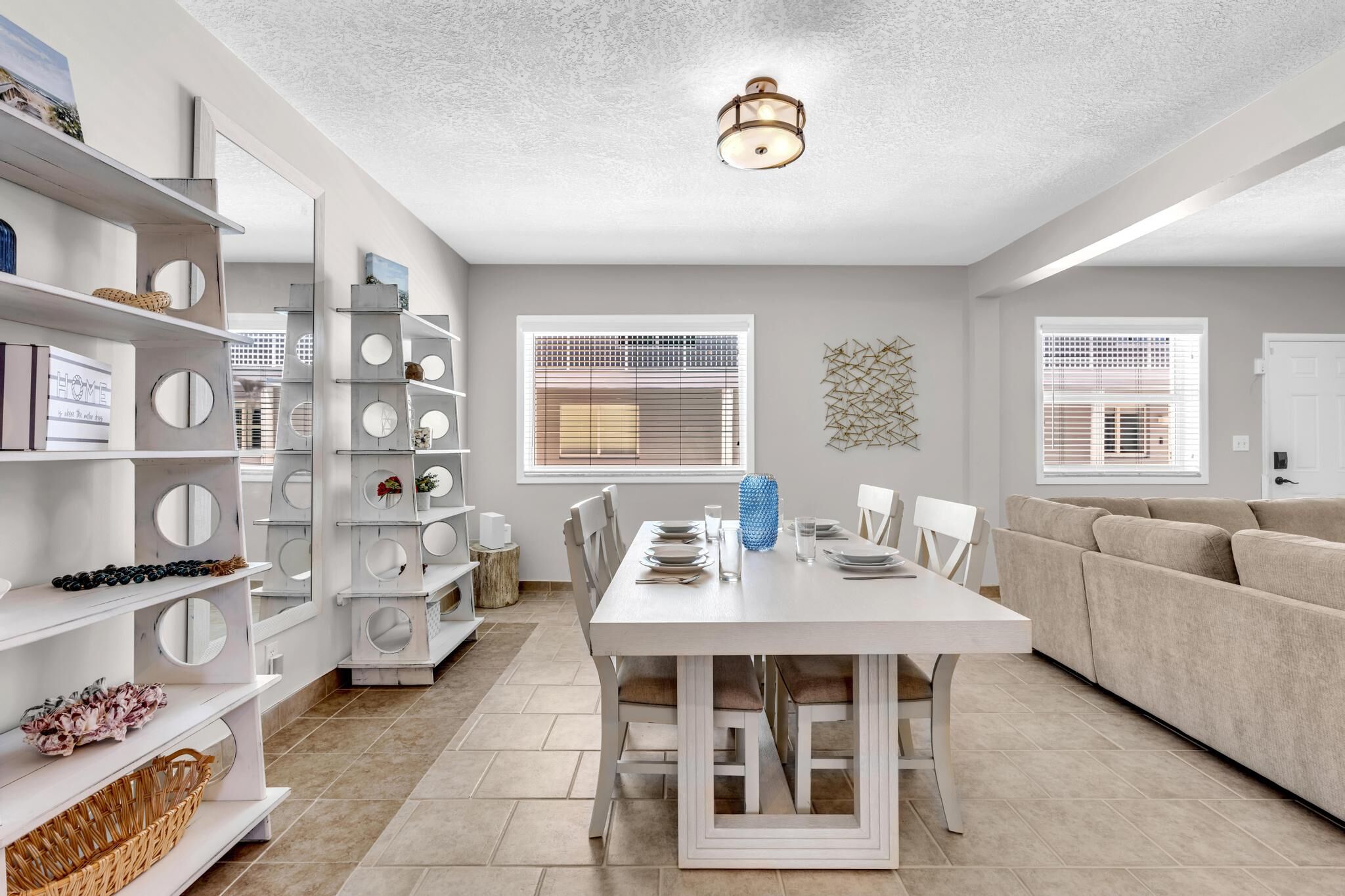 A modern living room with a dining area, white furniture, and a decorative wall piece.