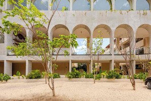 A modern building with multiple arches and a courtyard with trees and gravel. - DÉJÁ VU PH 410 By SANDY POWERFUL (Tulum)