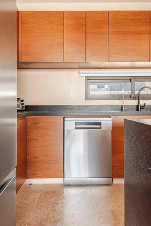 A kitchen with wooden cabinets, a stainless steel dishwasher, and a granite countertop. - DÉJÁ VU PH 410 By SANDY POWERFUL (Tulum)