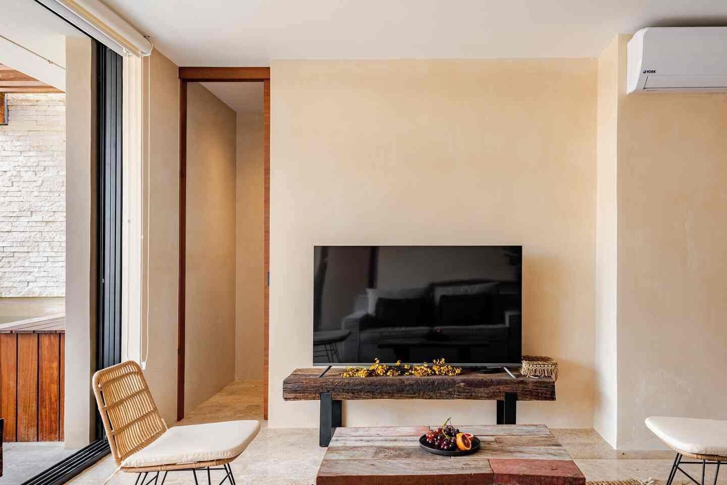 Una sala moderna con televisor de pantalla plana en la pared, una mesa de centro de madera con fruta y dos sillones.