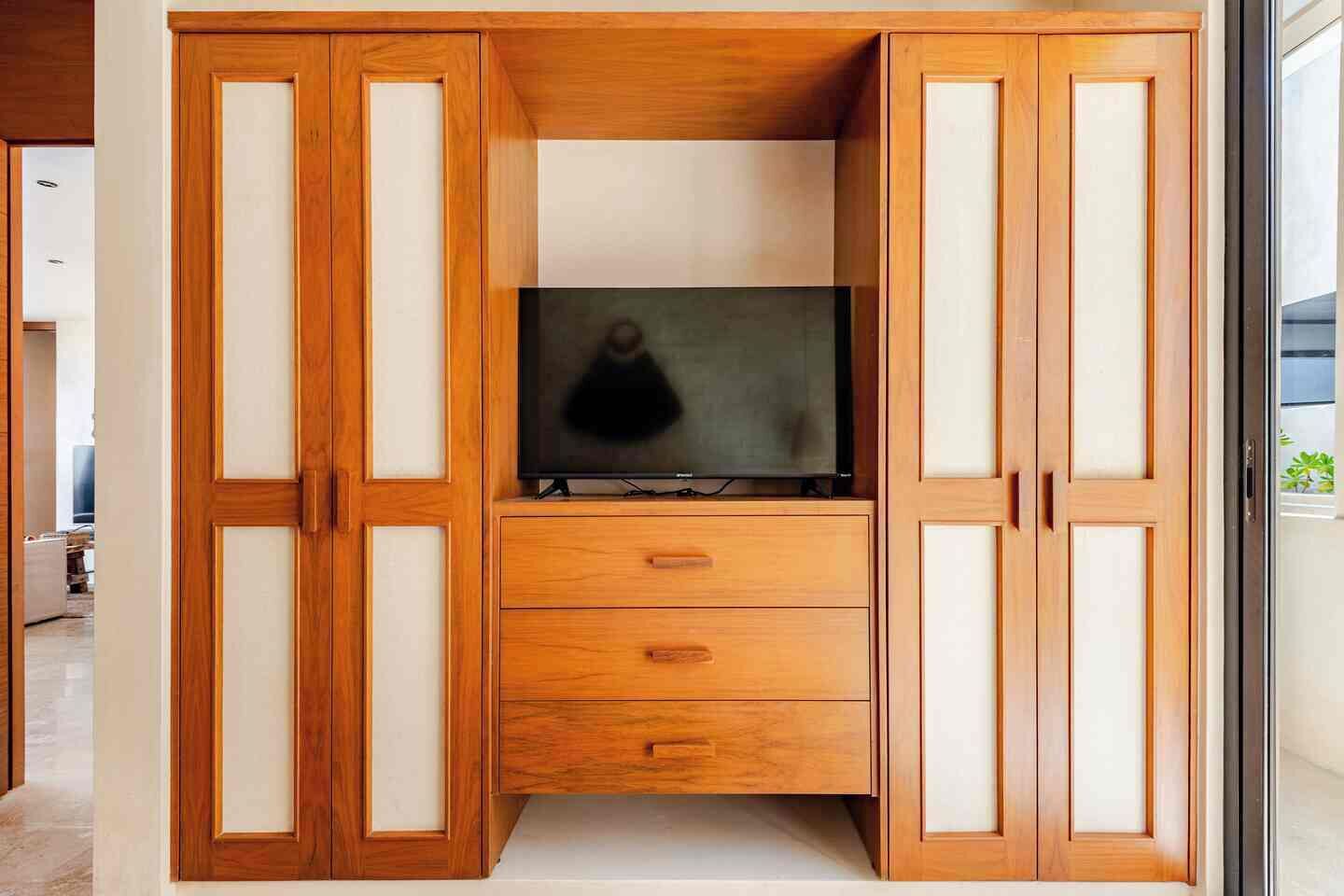 Un meuble en bois sur lequel est posée une télévision, avec des tiroirs et une porte en verre.