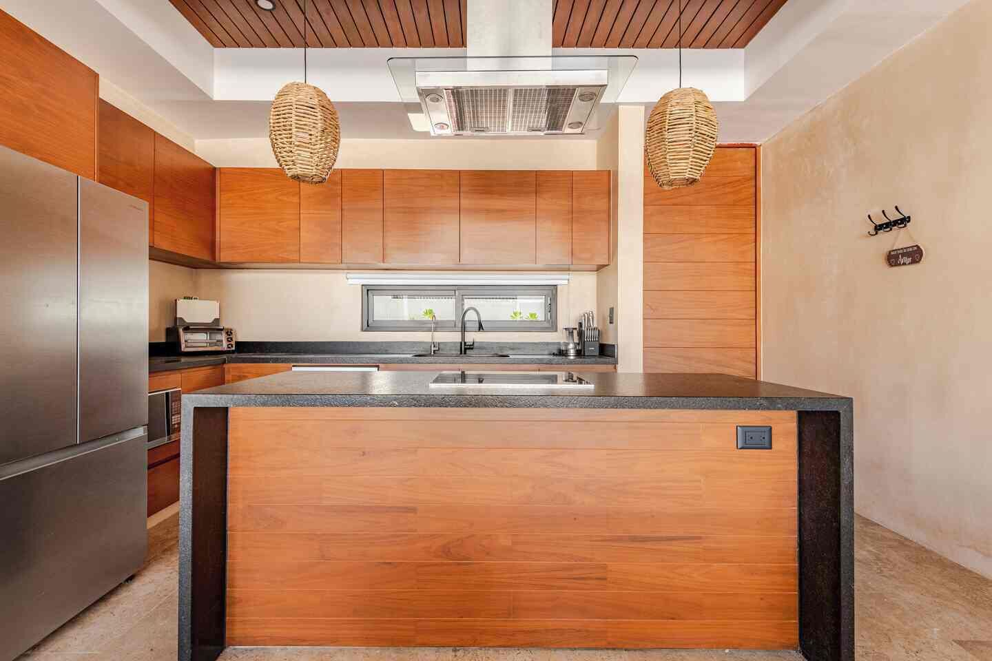 Une cuisine moderne avec des meubles en bois, un îlot central, des appareils en acier inoxydable et des suspensions lumineuses en fibres tressées.