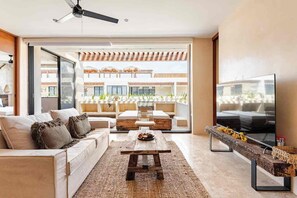 A modern living room with a sofa, coffee table, and TV, leading to an outdoor balcony with seating and plants. - DÉJÁ VU PH 410 By SANDY POWERFUL (Tulum)