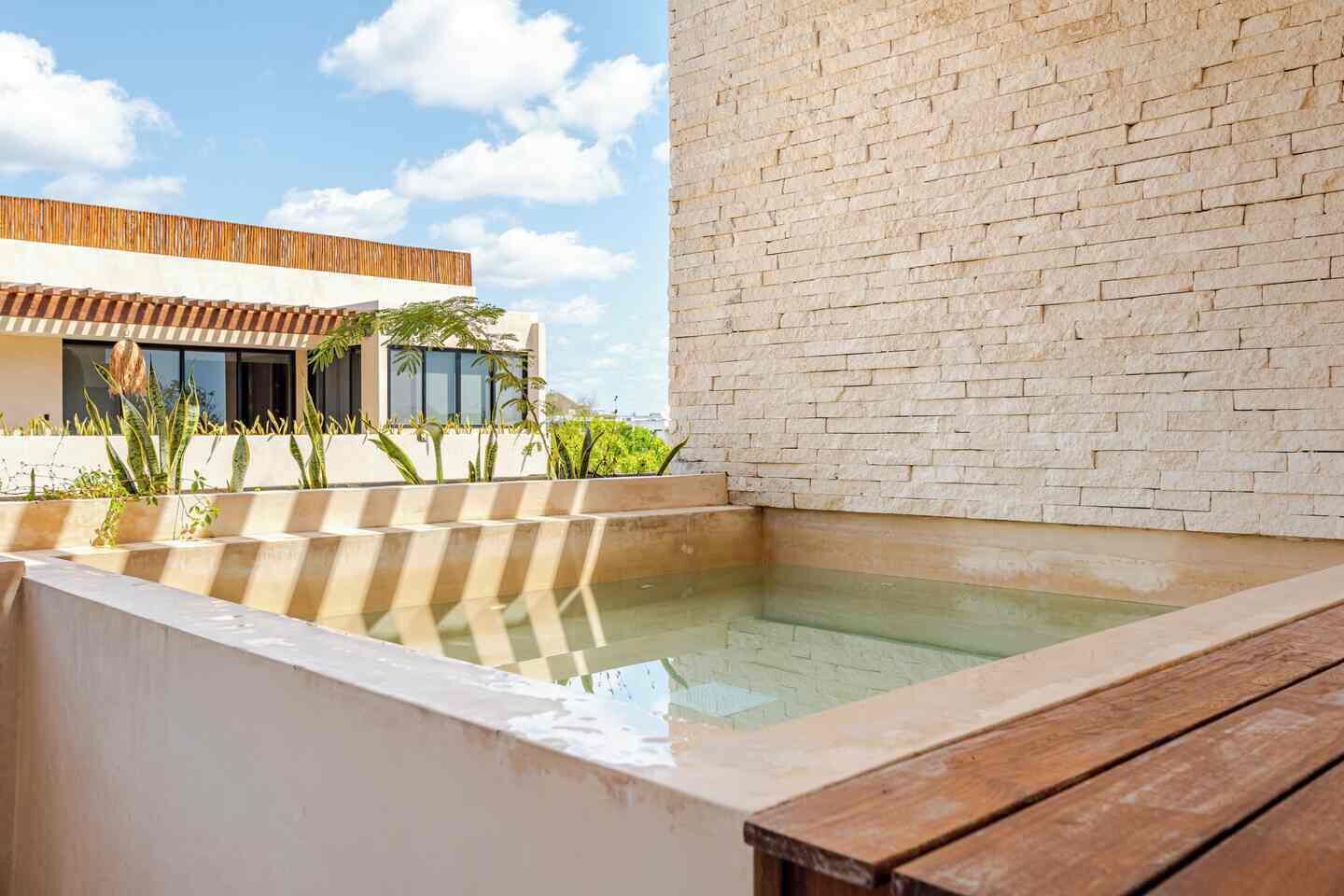 A spa area with a hot tub, a wooden bench, and a modern building with a brick wall in the background.