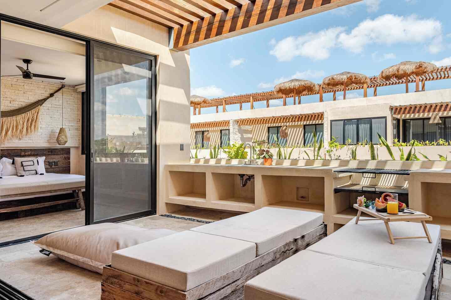 Una moderna area salotto all'aperto con divano, tavolo da pranzo con un vassoio di frutta e vista su una piscina con ombrelloni.