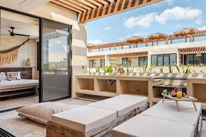 A modern outdoor seating area with a sofa, a dining table with a tray of fruit, and a view of a pool with umbrellas. - DÉJÁ VU PH 410 By SANDY POWERFUL (Tulum)