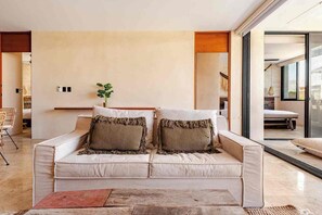 A modern living room with a sofa, two decorative pillows, a small plant, and a view through a glass door. - DÉJÁ VU PH 410 By SANDY POWERFUL (Tulum)
