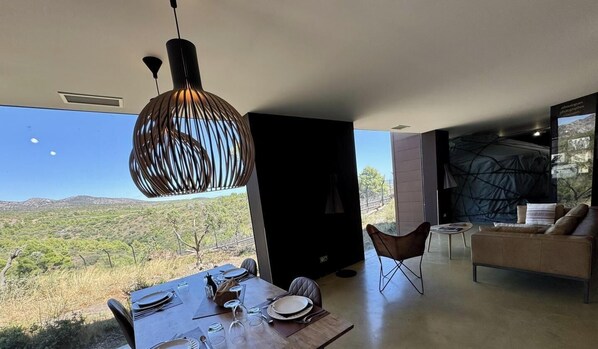 Un coin repas avec une table dressée pour deux personnes, un luminaire suspendu et une vue sur un paysage montagneux.