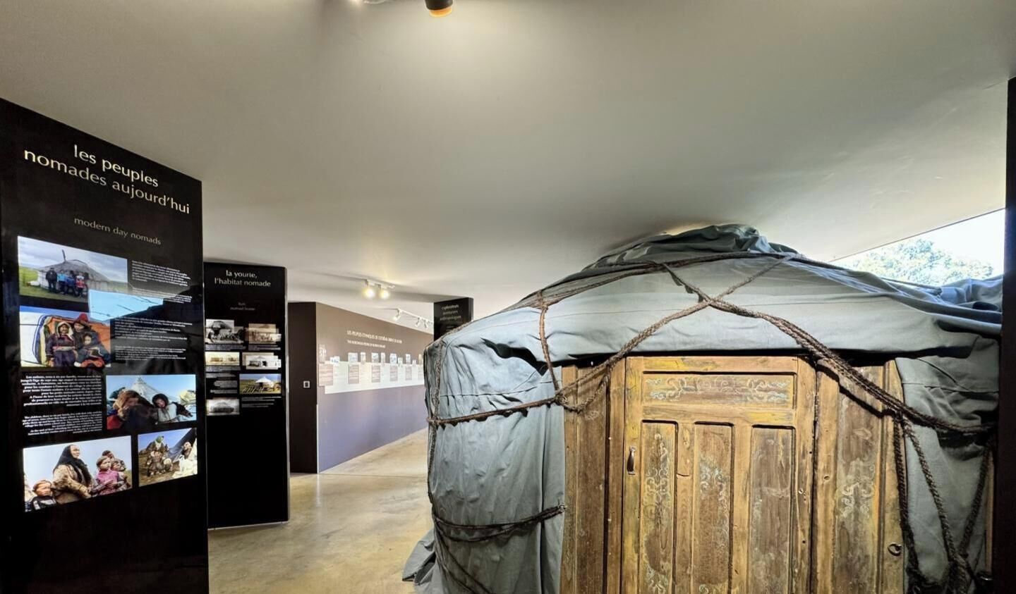 A museum exhibit with a nomadic tent structure, informational panels, and a wooden door.