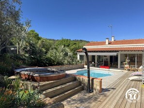 Ein Poolbereich mit Whirlpool, Holzterrasse und einem Haus mit Ziegeldach.