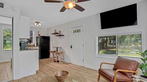 Ein geräumiger Wohnbereich mit Deckenventilator, einem an der Wand montierten Fernseher und Blick ins Freie durch ein Fenster.