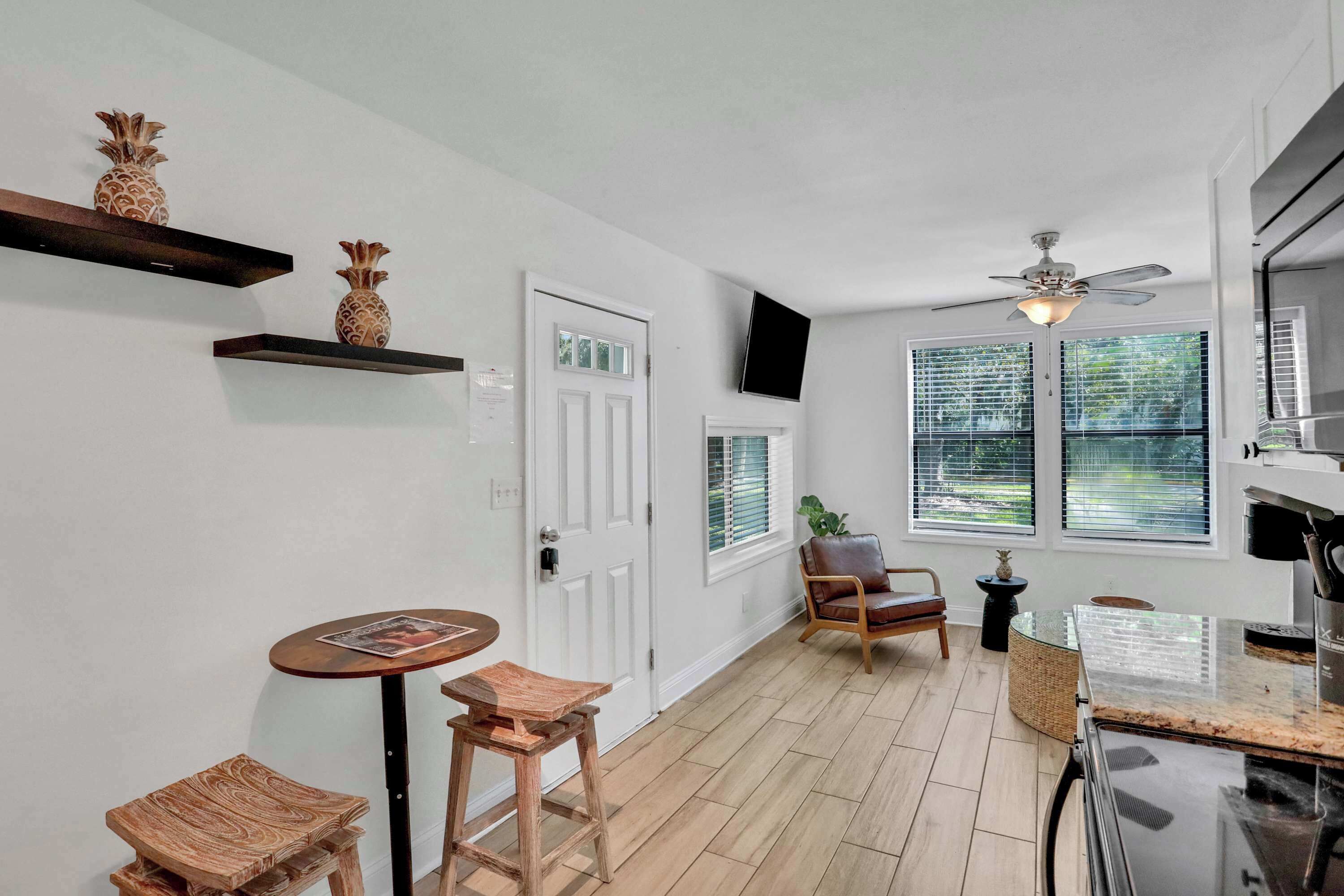 A kitchen with wooden flooring, a ceiling fan, a dining area with stools, and a window with blinds.