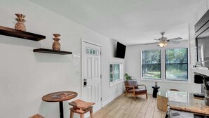 Eine Küche mit Holzboden, Deckenventilator, Essbereich mit Hockern und einem Fenster mit Jalousien.