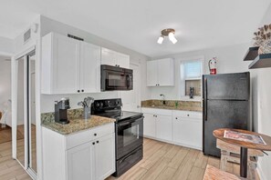 A modern kitchen with white cabinetry, a black refrigerator, a built-in microwave, a stove, and a coffee maker.