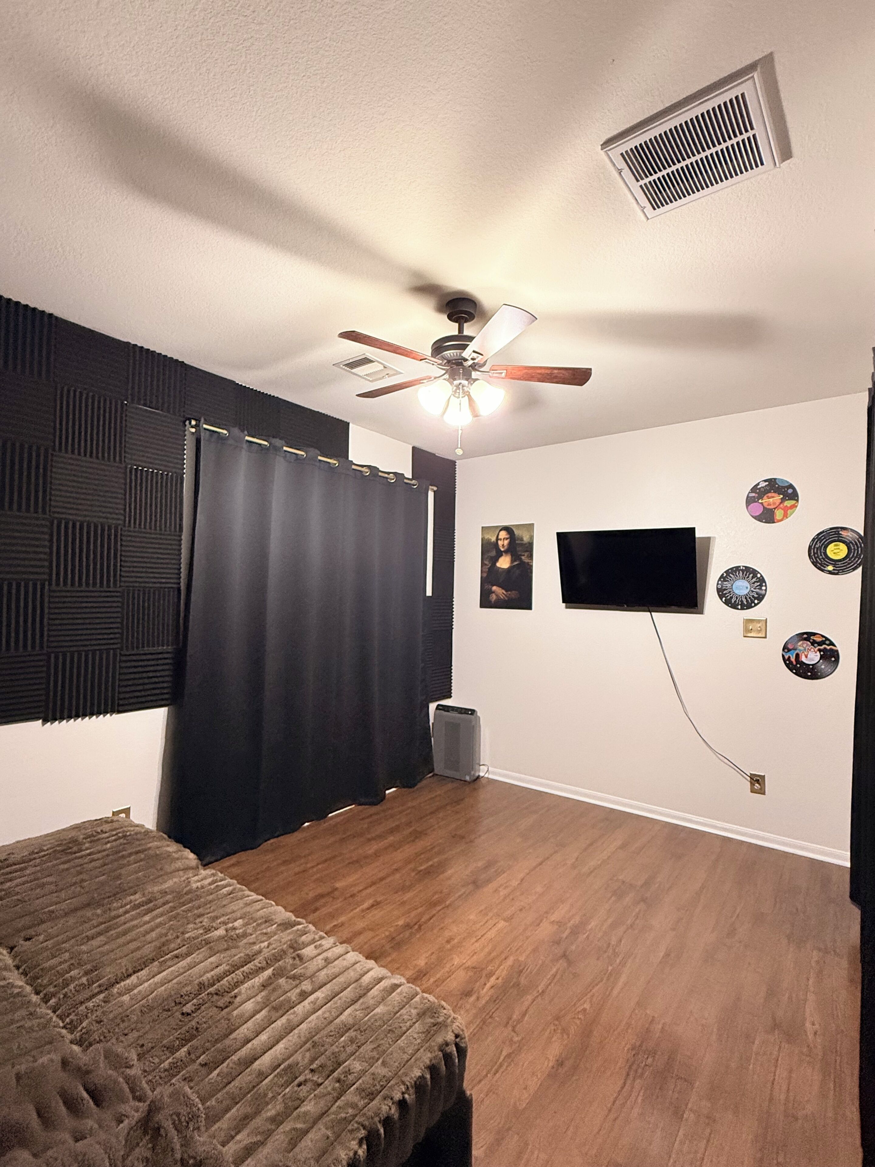 Un dormitorio con cama, ventilador de techo, televisor montado en la pared y paneles insonorizados.