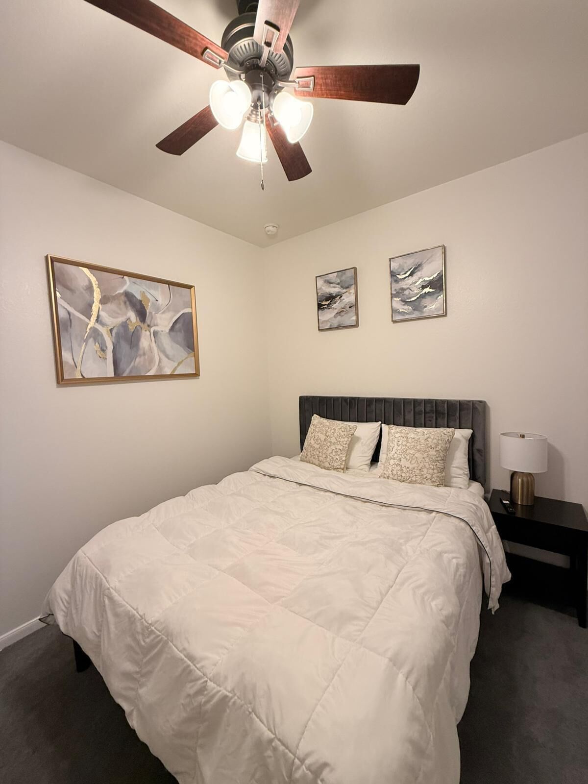 A bedroom with a bed, a ceiling fan, and artwork on the walls.