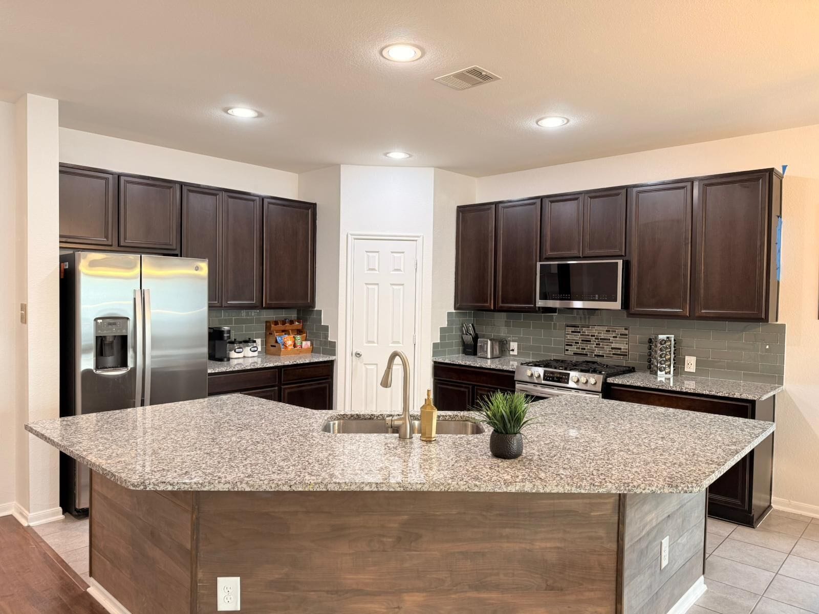 A modern kitchen with dark wood cabinets, stainless steel appliances, and a granite island.