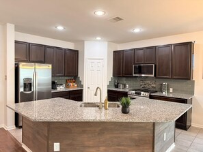 A modern kitchen with dark wood cabinets, stainless steel appliances, and a granite island. - Cozy Katy Getaway • 5 Min to Shops & Dining (Katy)
