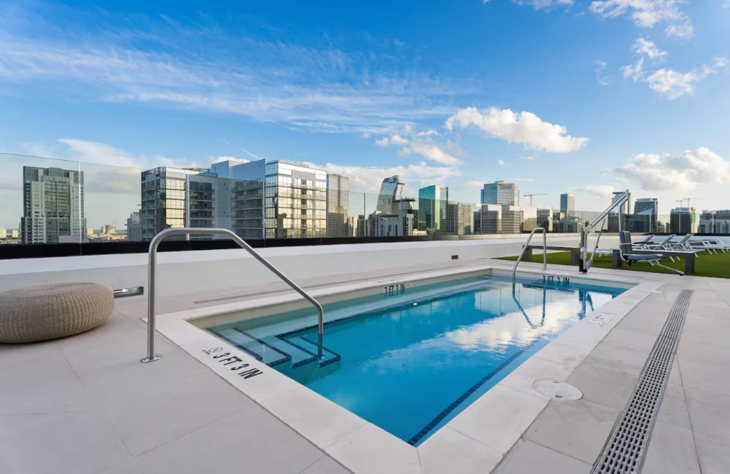 A rooftop swimming pool with a city skyline view, surrounded by modern buildings.