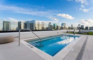 Une piscine sur le toit offrant une vue panoramique sur les gratte-ciel de la ville, entourée de bâtiments modernes.