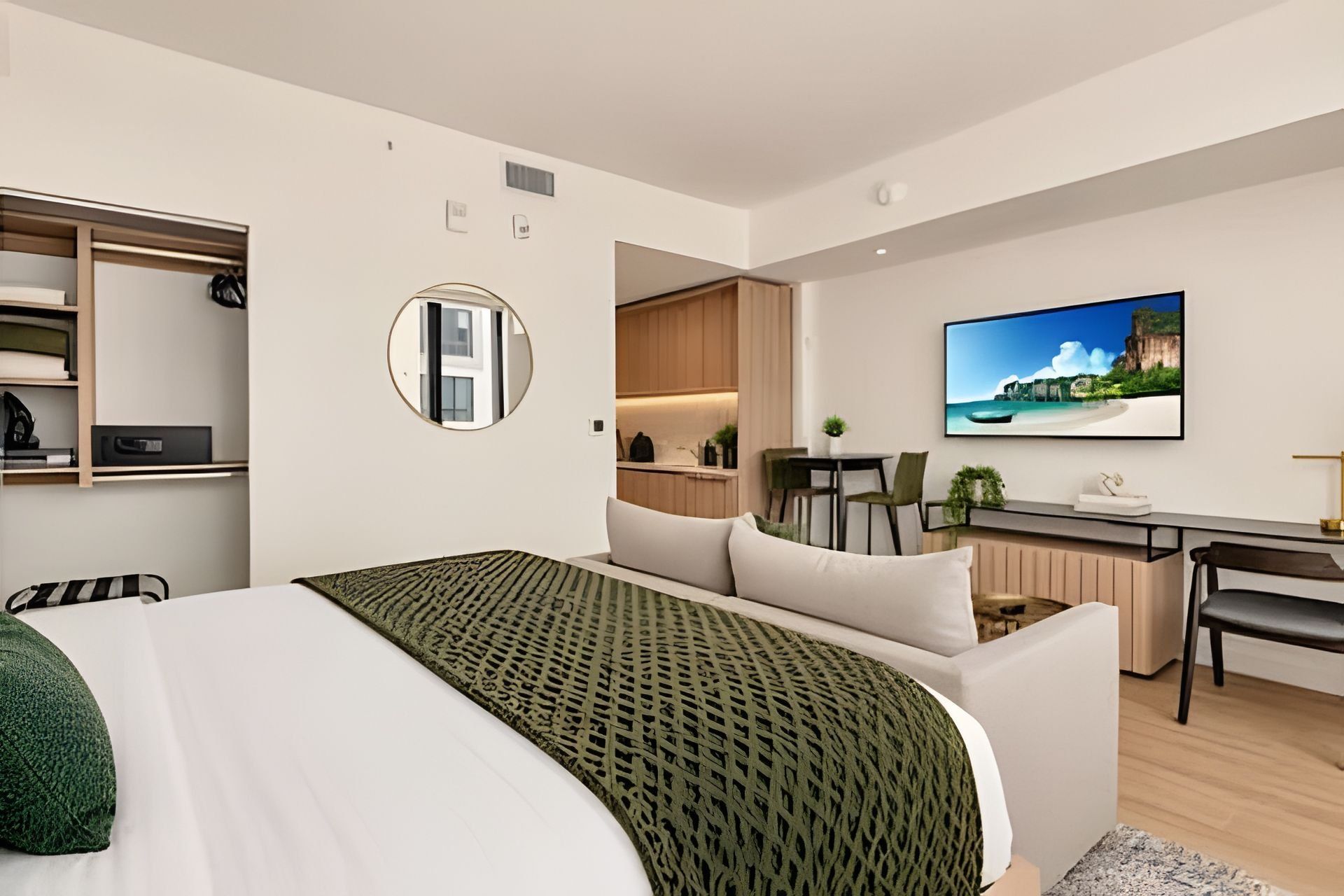 Quarto de hotel moderno com cama, escrivaninha, cozinha compacta e uma grande janela.