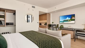 Quarto de hotel moderno com cama, escrivaninha, cozinha compacta e uma grande janela.