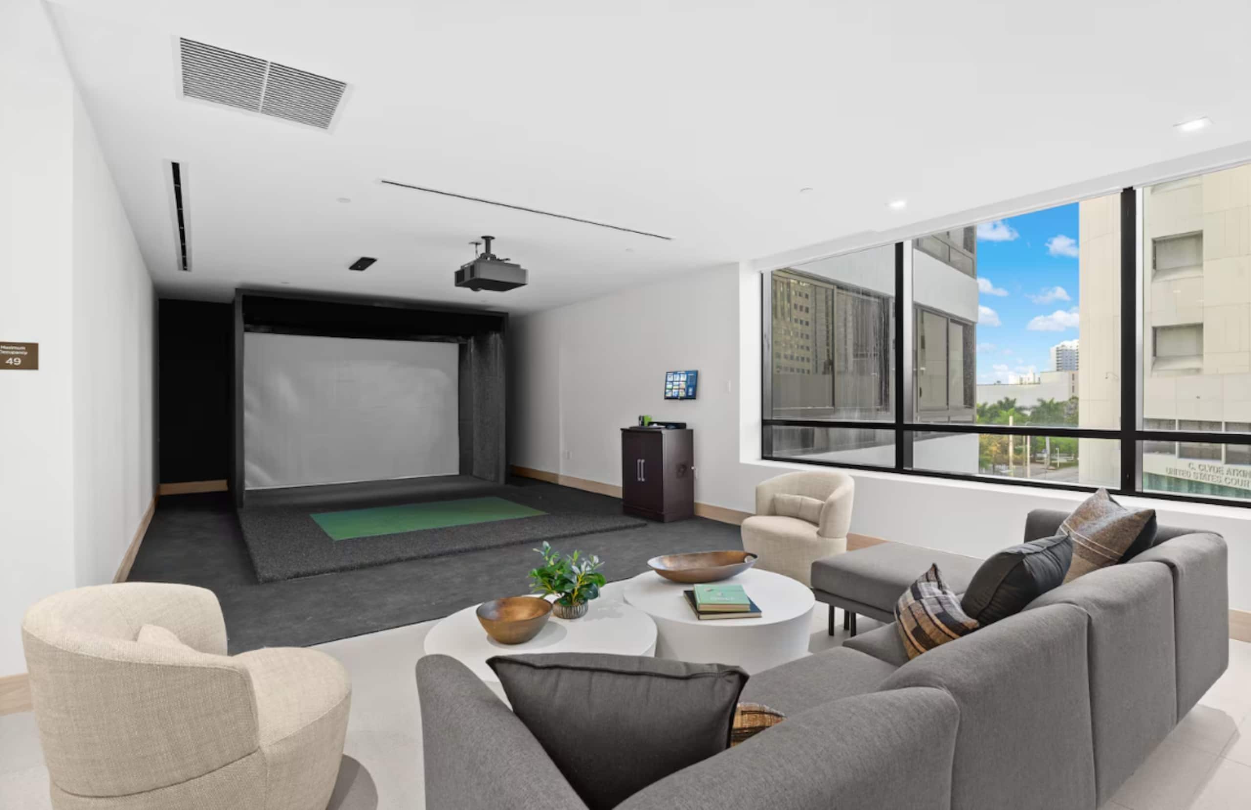A modern living room with a flat-screen TV, comfortable seating, and a large window offering a city view.