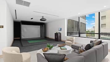 A modern living room with a flat-screen TV, comfortable seating, and a large window offering a city view.