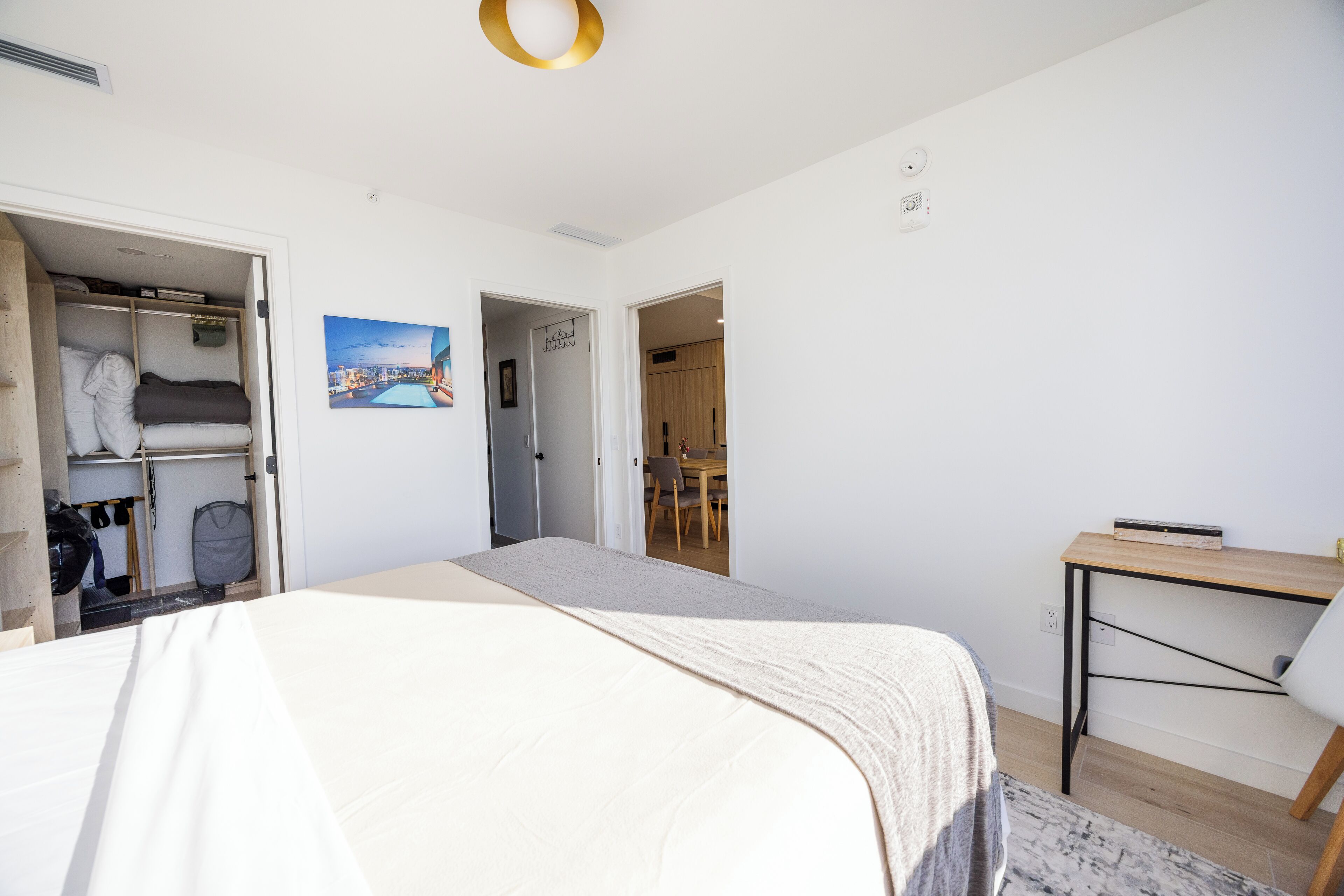 Un dormitorio con cama, armario, un cuadro y escritorio con silla.