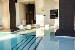 A clear indoor swimming pool with marked lanes, a sign indicating pool rules, and a restroom sign. - District 3704 (Miami)