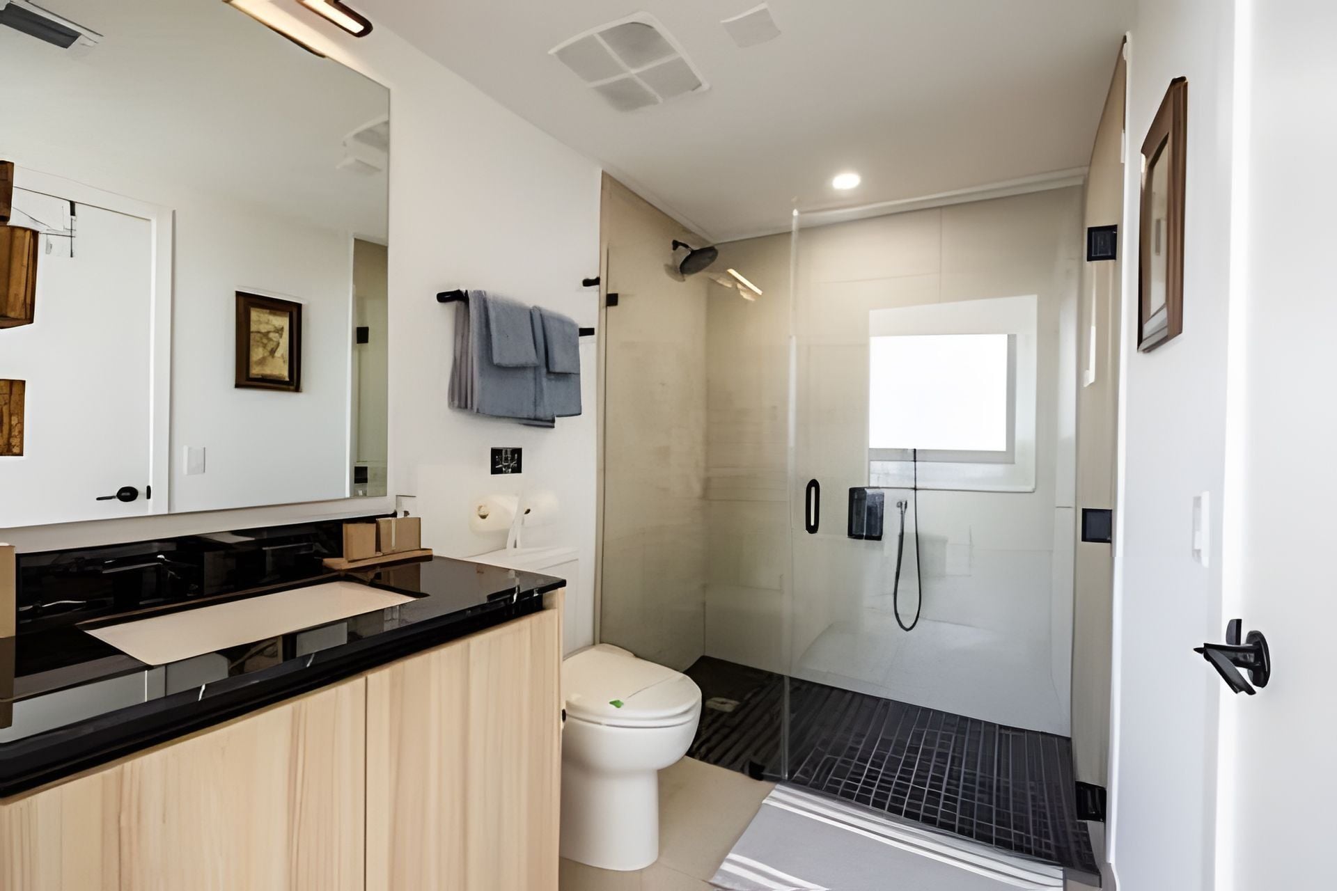 Uma casa de banho moderna com bancada preta, sanita branca, chuveiro com divisória de vidro e um espelho grande.