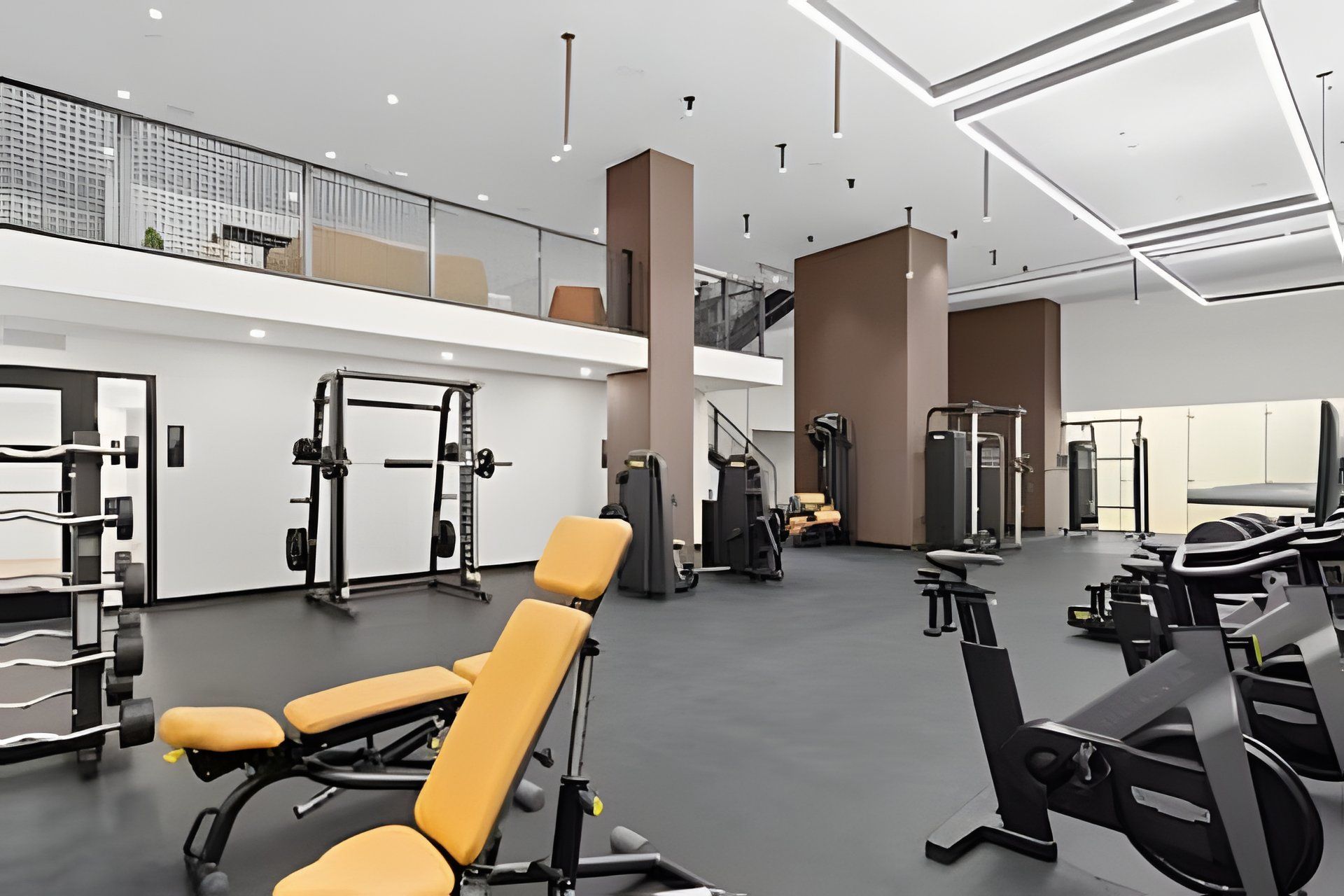 A modern gym with various exercise equipment, a mezzanine level, and a spacious layout.
