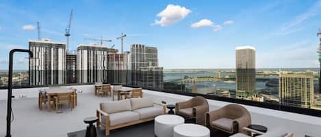A rooftop terrace with outdoor seating, a view of a city skyline, and construction cranes in the background.